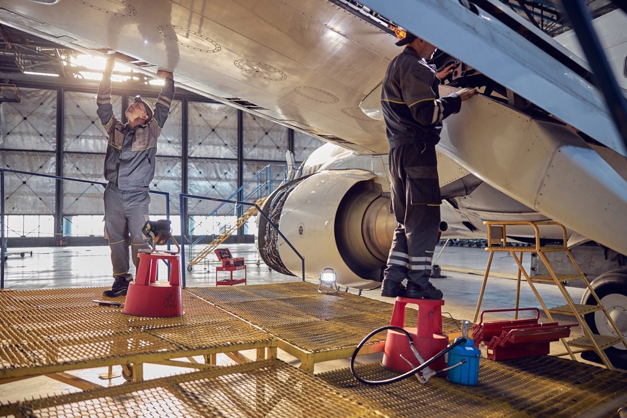 Full length side view portrait of men aviation mechanics fixing and checking spoiler and flaps on the airplane